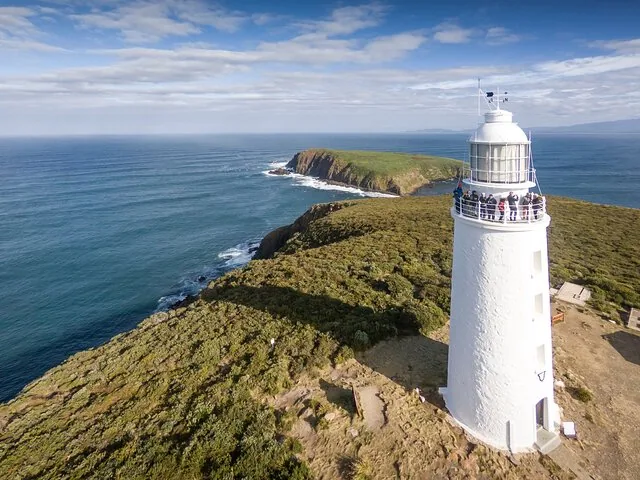 Vue aérienne du phare de Cape Bruny avec des touristes sur le balcon et paysage côtier.