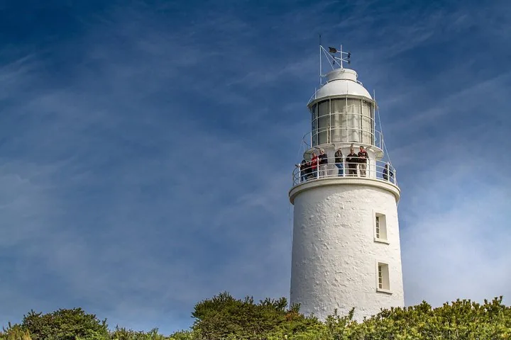 Turistas parados en el balcón del faro de Cape Bruny bajo un cielo azul.